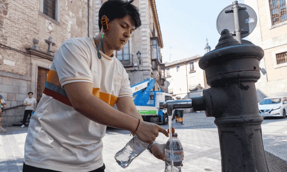 Un chico rellena botellas de agua en una fuente para hidratarse en Toledo.