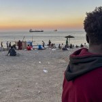 Grupos de personas migrantes en la playa El trampolín de Ceuta al atardecer.