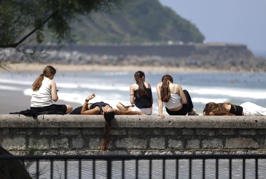 Unas jóvenes toman el sol junto a la playa de la Zurriola de San Sebastián.