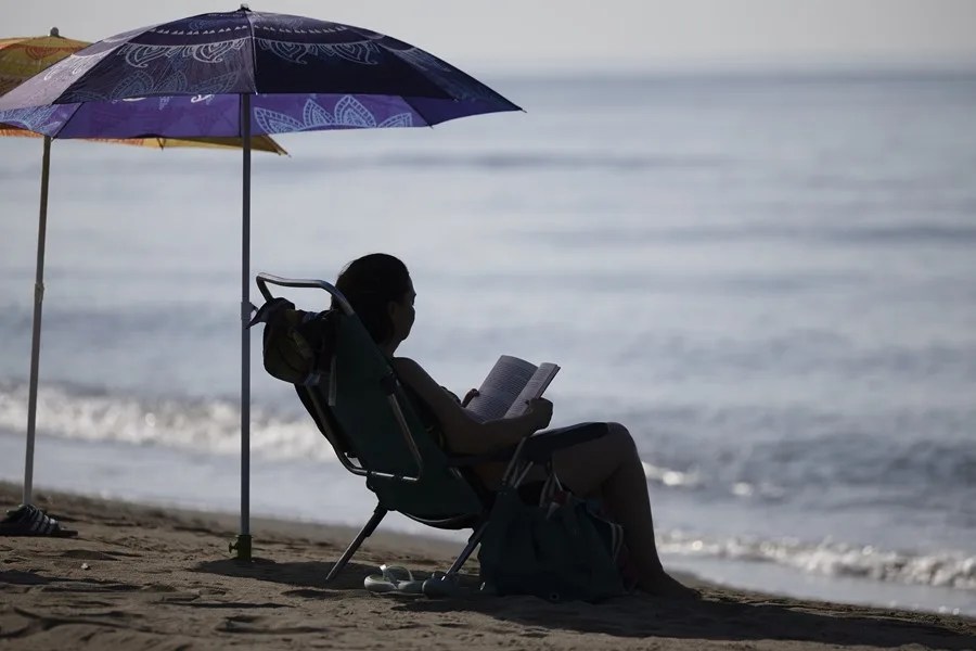 Una mujer lee bajo la sombra de una sombrilla en la playa del Rincón de la Victoria (Málaga).