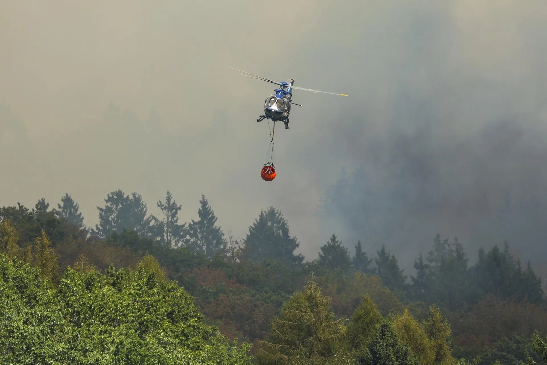 DUEREN (Germany), 14/08/2026.- A police helicopter fights the wildfire at the Huertgenwald near Dueren, Germany, 14 August 2026. EFE/EPA/CHRISTOPHER NEUNDORF