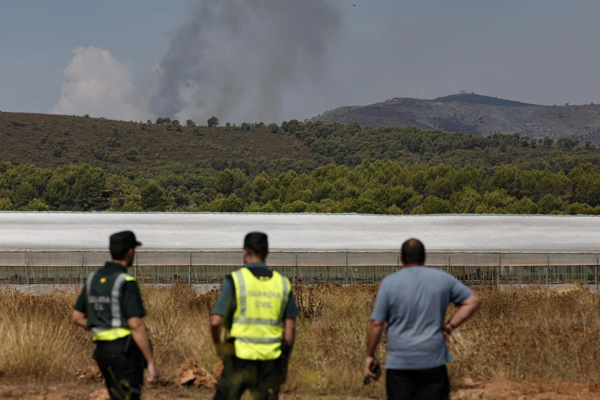 GRAFCVA5489. SEGORBE (CASTELLÓN), 21/08/2026.- El incendio forestal declarado ayer por la tarde en Segorbe (Castellón), cerca del parque natural de la Calderona, avanza sin control tras afectar ya a unas 120 hectáreas mientras los equipos de extinción buscan aprovechar esta mañana las condiciones meteorológicas antes de que cambien al mediodía. En la imagen dos guardias civiles y un vecino de segorbe observan el frente del incendio. EFESManuel Bruque