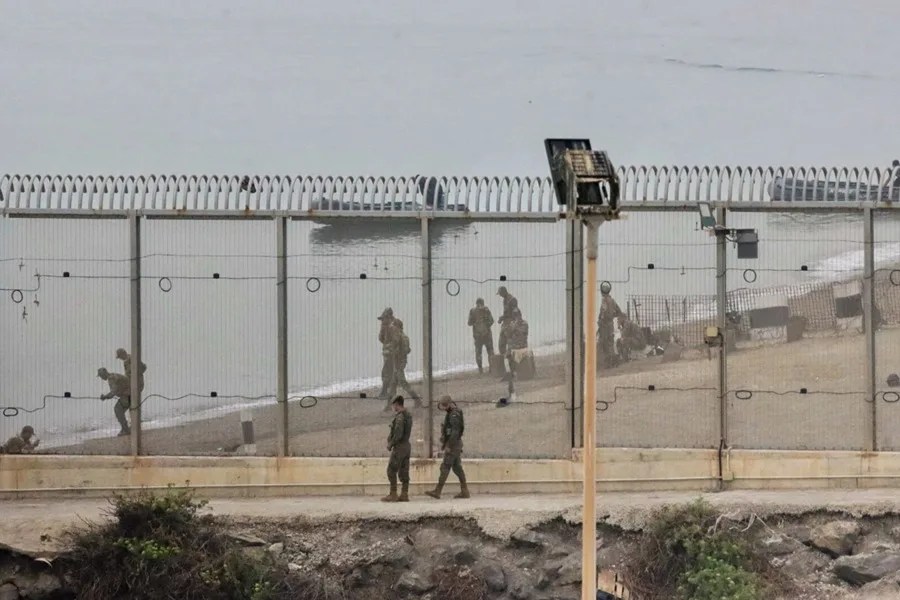 Dos soldados españoles y en la parte marroquí de la playa autoridades del país vecino montan guardia en el espigón del Tarajal que separa Ceuta de Marruecos.