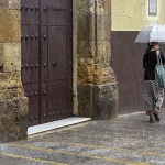 Una mujer se refugia con un paraguas en Sevilla.