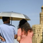 Una pareja pasea por Sevilla bajo una sombrilla, este jueves.
