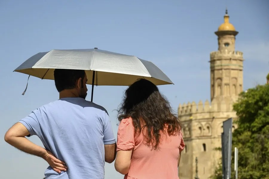 Una pareja pasea por Sevilla bajo una sombrilla, este jueves.