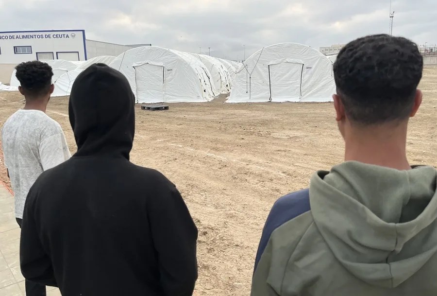 Tres jóvenes migrantes esperan en la mañana de este lunes para ser alojados en el nuevo campamento