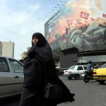 Una mujer iraní con velo pasa junto a una valla publicitaria antiamericana en Teherán, Irán