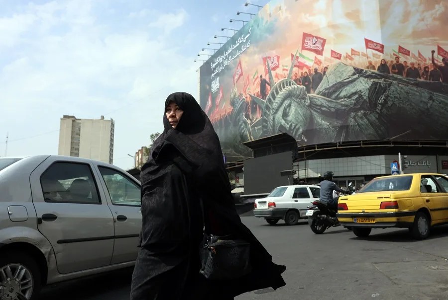 Una mujer iraní con velo pasa junto a una valla publicitaria antiamericana en Teherán, Irán