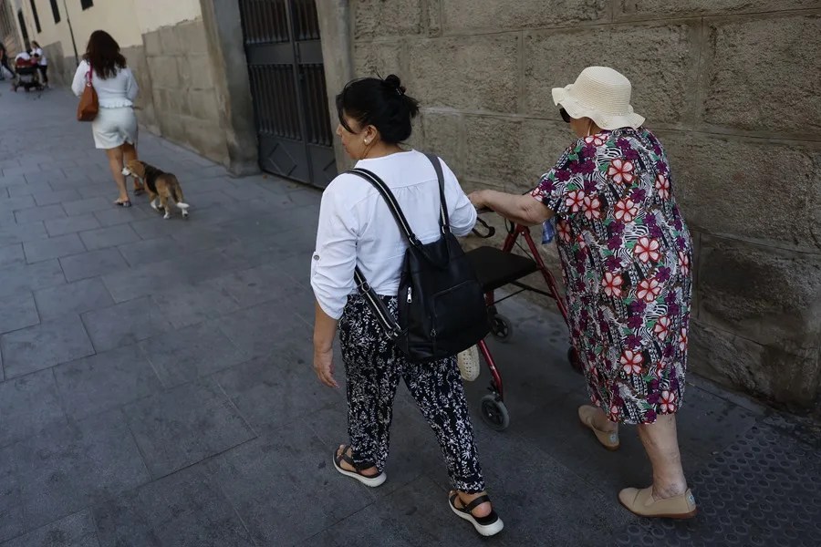 Una mujer mayor pasea con su cuidadora con ayuda de un andador.