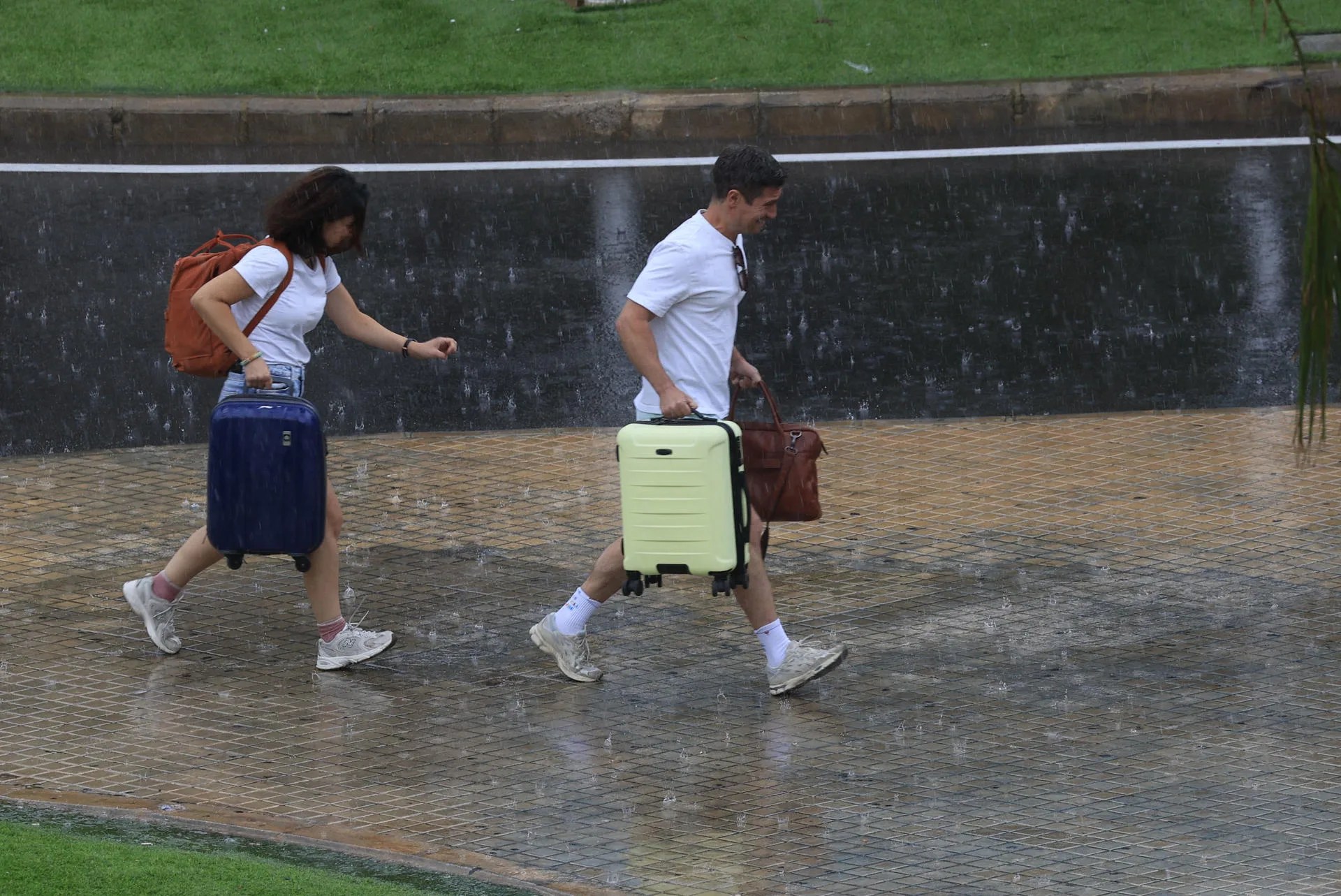 Dos personas con equipaje caminan bajo la lluvia en el aeropuerto de Manises (València). Archivo/ EFE/ Kai Forsterling