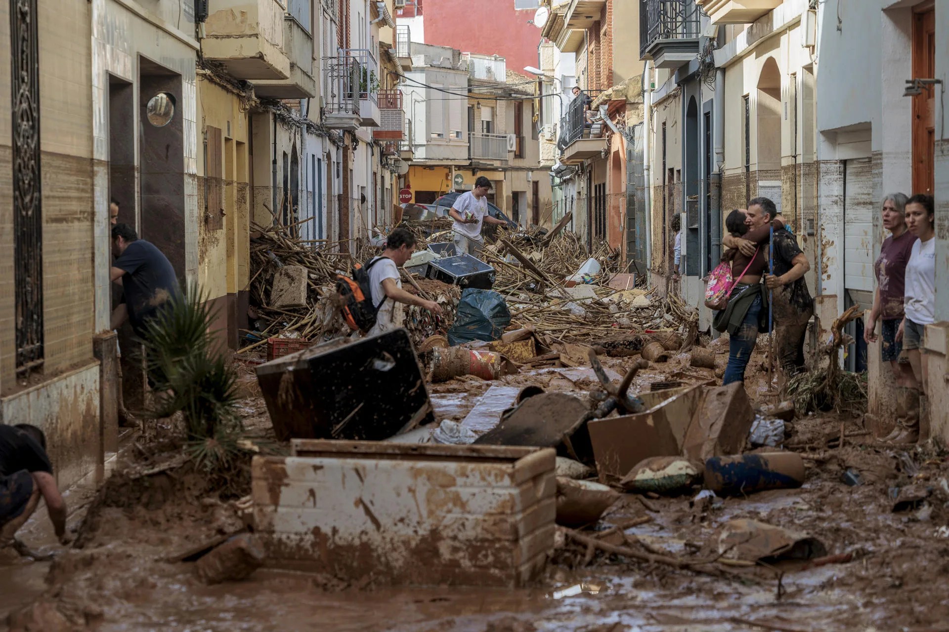 Vecinos intentan atravesar una calle en Paiporta cubierta de barro y enseres dos días después de la dana. EFE/ Biel Aliño
