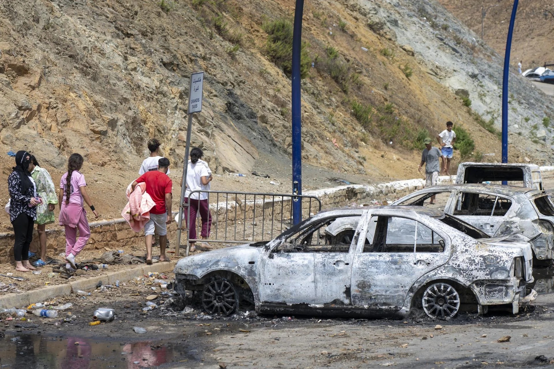 (FILE).- People walk past burnt out cars at the site of clashes near the Bab Sebta border crossing near Fnideq, Morocco, 31 July 2026. EFE/EPA/JALAL MORCHIDI