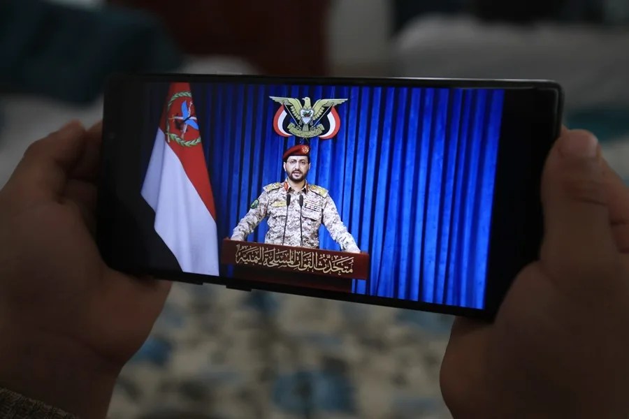 Una persona observa un teléfono móvil que muestra al portavoz militar hutí, Yahya Sarea, emitiendo una declaración en Saná