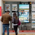 Una pareja se detiene a observar las propiedades en venta anunciadas en el escaparate de una agencia inmobiliaria de Menorca