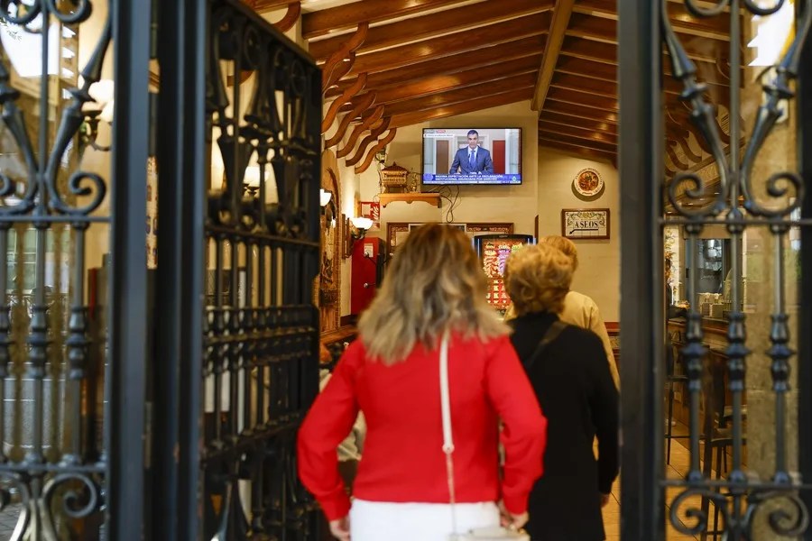 Varias personas siguen la comparecencia del presidente del Gobierno, Pedro Sánchez, desde un bar en Príncipe Pío, Madrid.