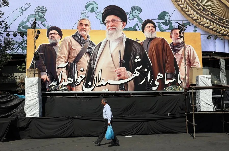 Un hombre iraní camina junto a una valla publicitaria que muestra una imagen del difunto Líder Supremo de Irán, el ayatolá Ali Jamenei (centro), y de líderes de Hamás, en una calle de Teherán.