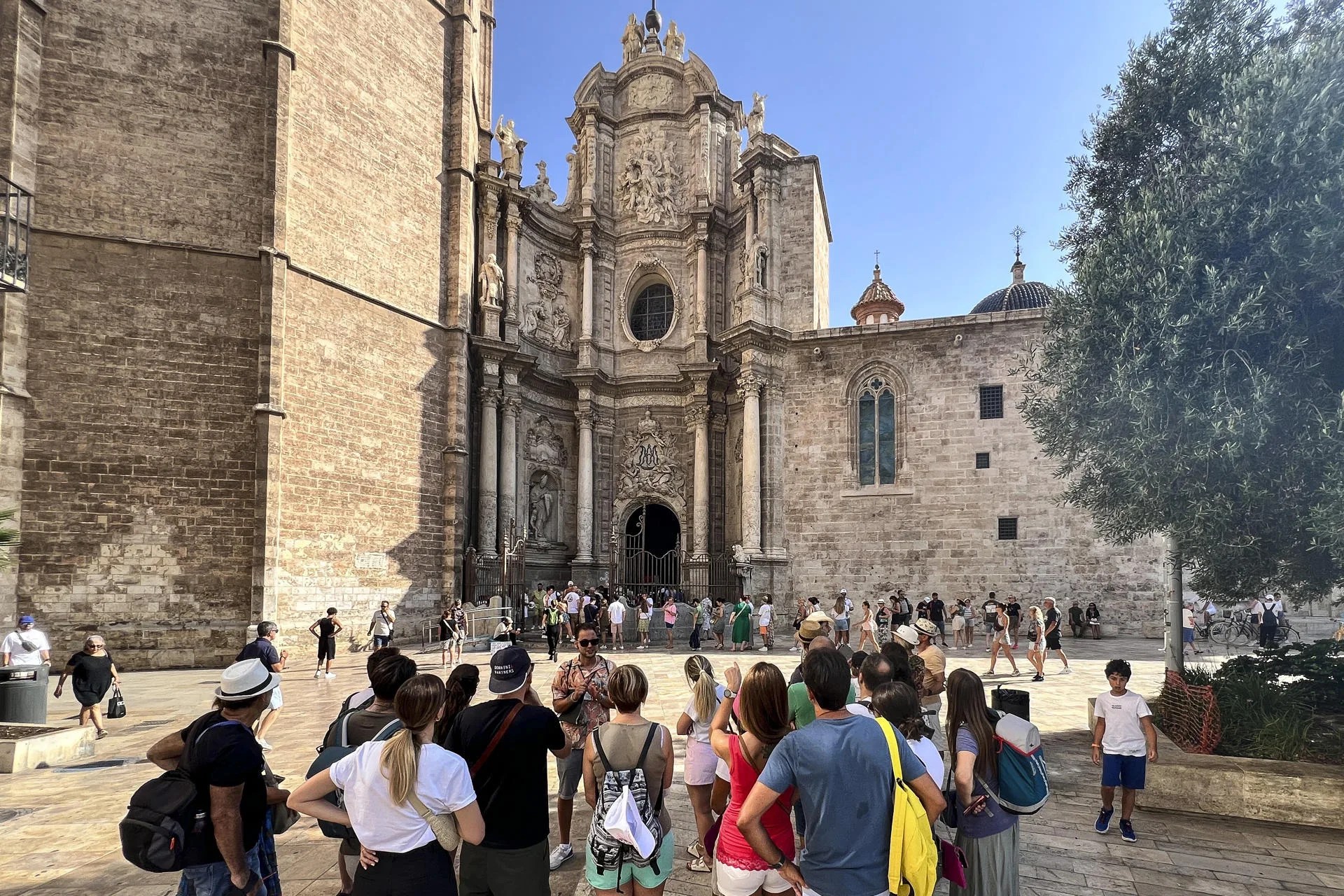 Un grupo de turistas escucha las indicaciones de su guía, mientras otros hacen cola para entrar a la catedral de València. EFE/Manuel Bruque