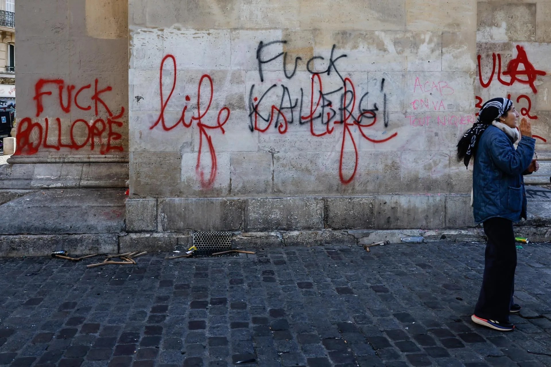 A woman stands next to graffiti written on a building facade in the aftermath of clashes between riot police and demonstrators in Paris, France, during nationwide protests against the high cost of living in the country, 18 October 2026. EFE-EPA/MOHAMMED BADRA