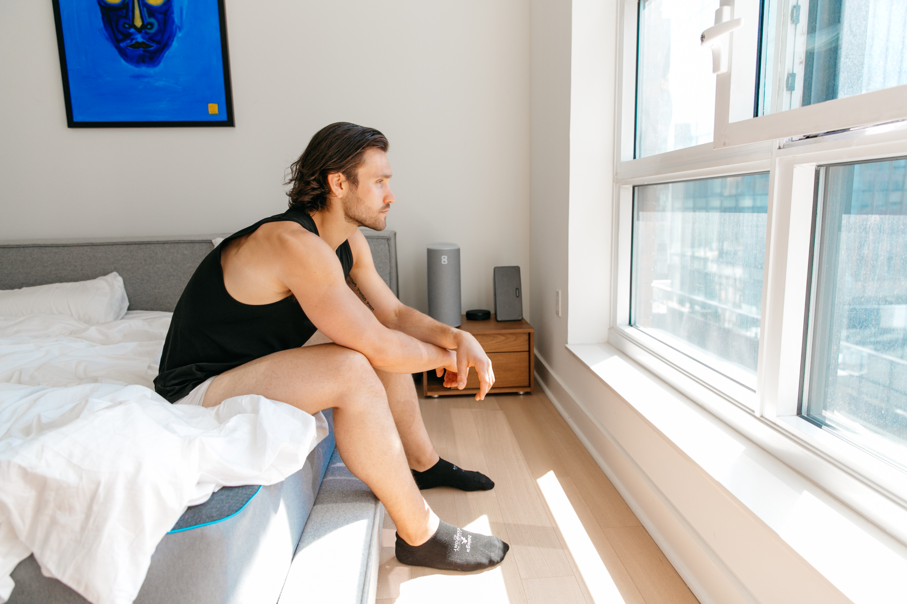 man looking out window sitting on bed