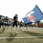 people in black uniform holding blue flag running on football field