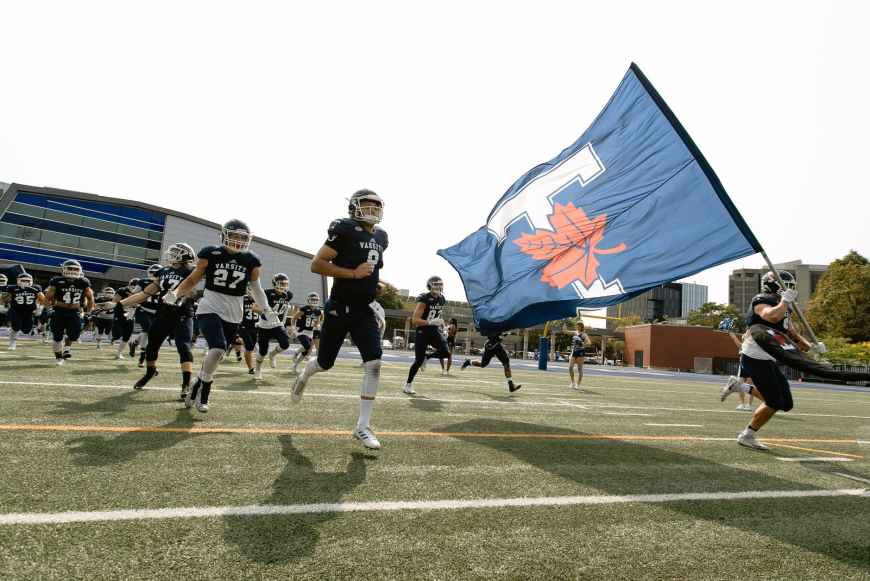 people in black uniform holding blue flag running on football field