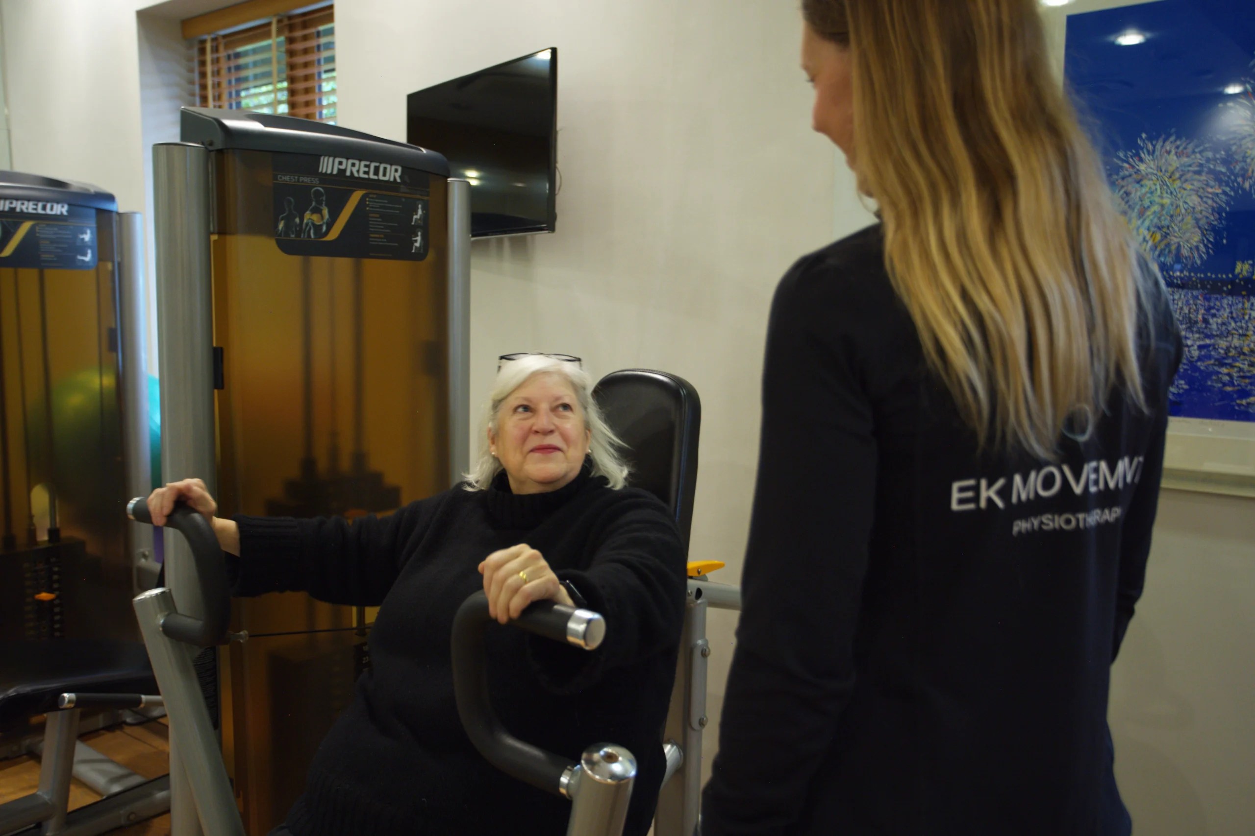 Physiotherapist Ellie Kis supervising an older female client as she performs a chest press exercise on a machine in the gym.