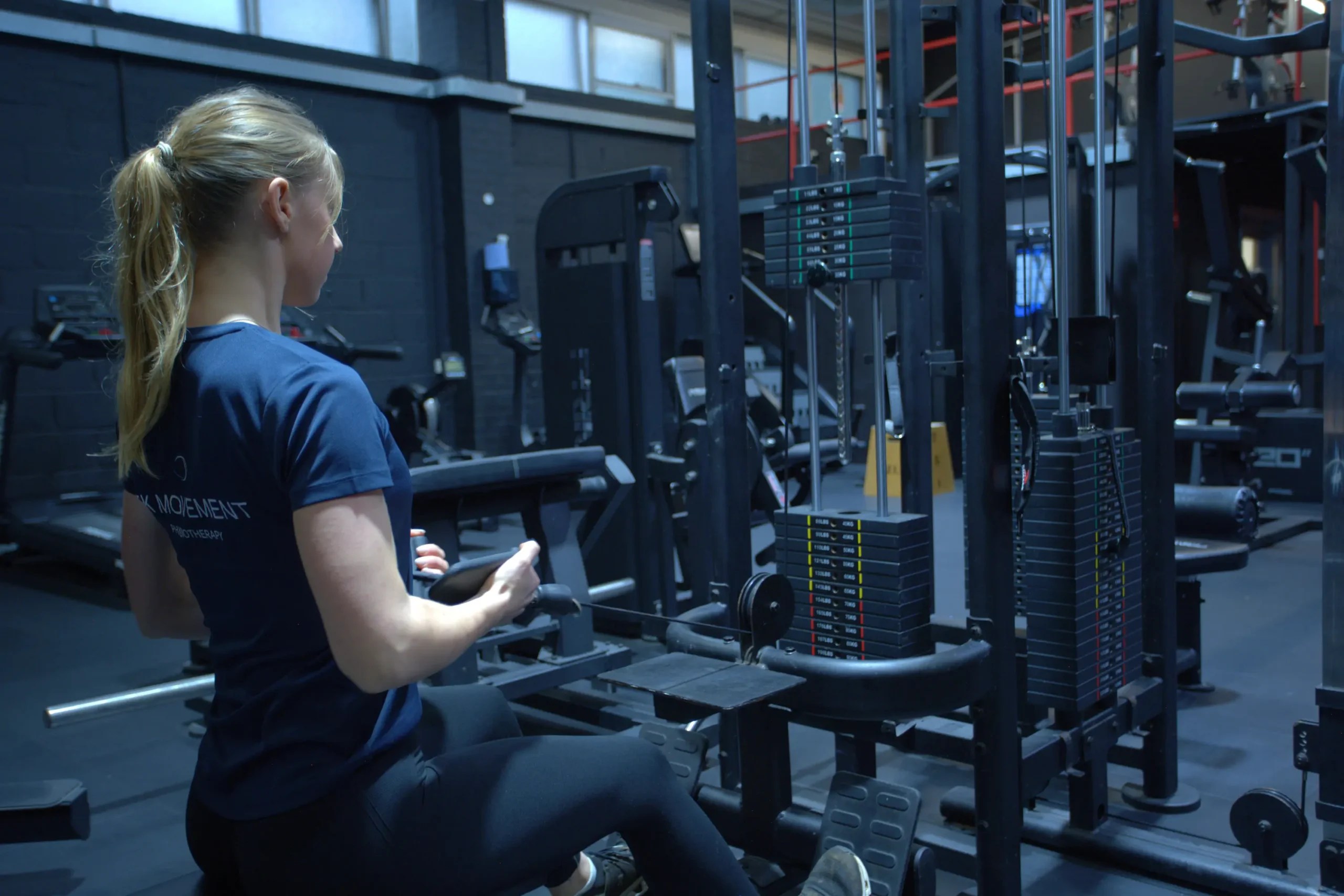 Physiotherapist Ellie Kis demonstrating a seated cable row exercise in the gym, highlighting the strength training focus of her custom rehabilitation programming.