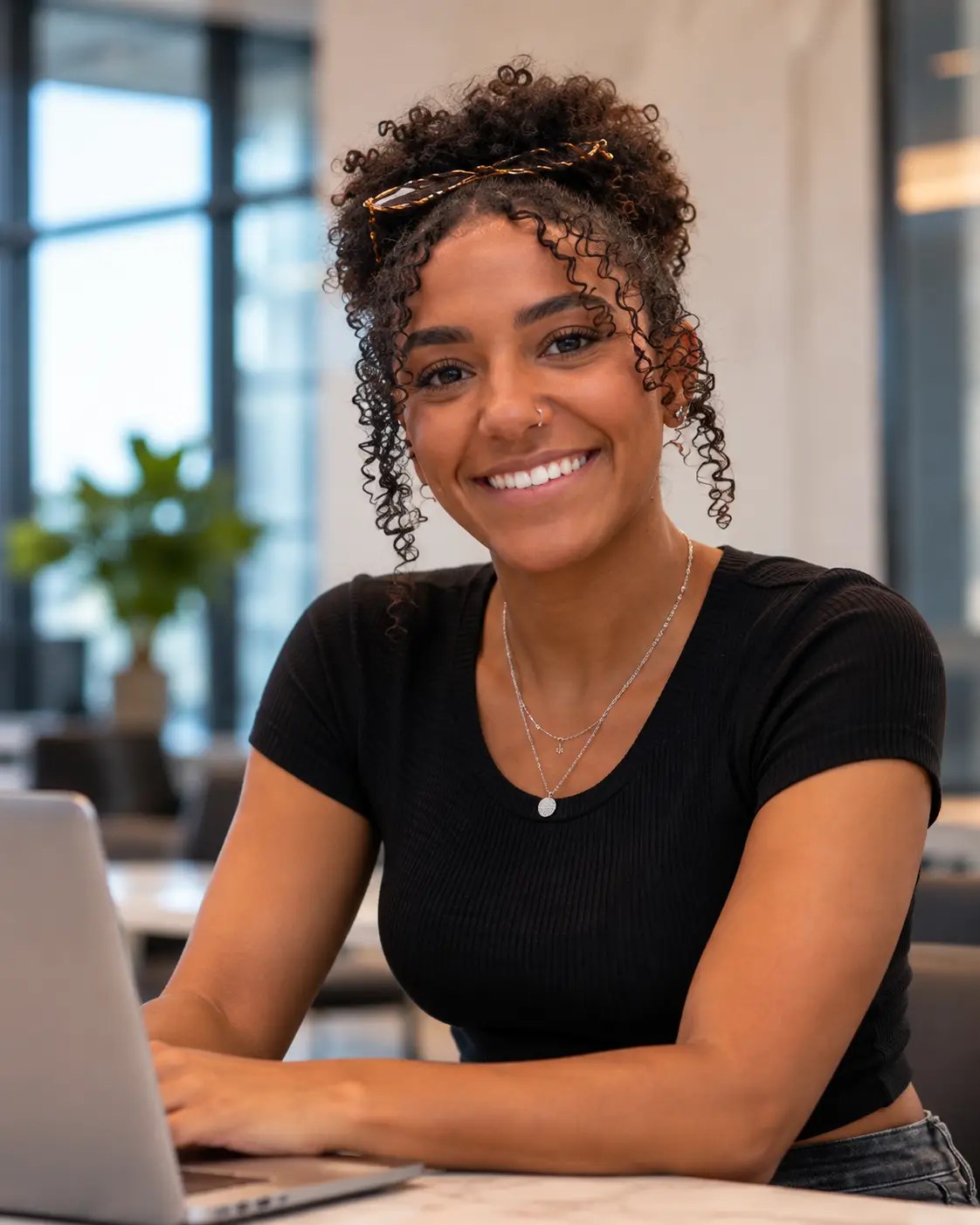 Farida smiling while working on a laptop in a modern office