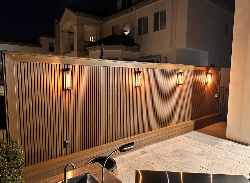 Four illuminated wall sconces mounted on a wood-slat outdoor patio wall
