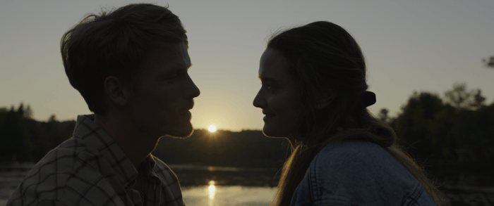 Silhouette of a man and woman facing each other against a sunset by water, with soft orange and yellow light illuminating the scene.