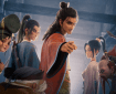 A group of animated characters from "ALL WISHES COME TRUE," with a central figure pointing forward and six others in various traditional attire, set in a dimly lit interior.