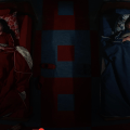 Two individuals in separate beds, a girl in red with a stuffed animal on the left and a boy in blue with a stuffed animal on the right, in a colorful room with a geometric floor pattern.