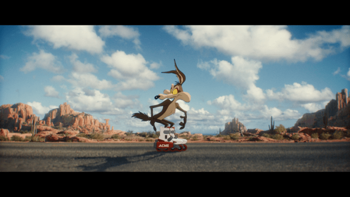 Wile E. Coyote wearing roller skates on a desert road, with red rock formations and a blue sky in the background.