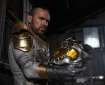 A man in the White Dragon costume holds a metallic helmet resembling a dragon's head in a dimly lit industrial setting.