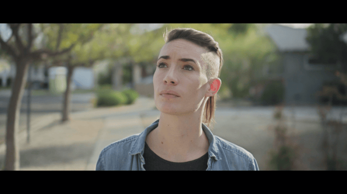 Close-up of a young adult in a denim shirt looking upward in a sunlit outdoor courtyard.