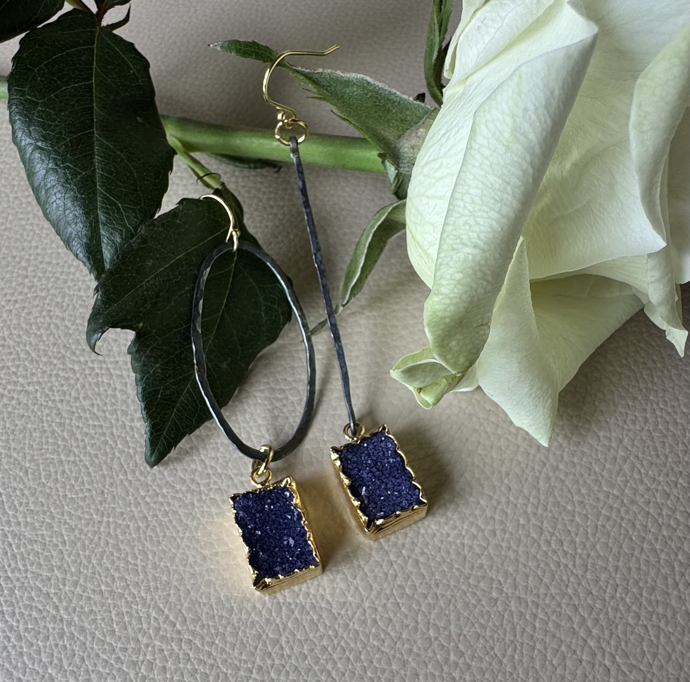 Asymmetric Mixed Metal Navy Blue Druse Quartz Earrings. Rectangular shaped blue druses are set in textured gold-plated bezel. The stones are suspended from contrasting hand hammered black oval rings and a bar. One earring is attached to a hand forged and textured oxidized silver oval ring and another to a long-oxidized silver bar. Finished with 14K gold filled French wire. The simple design of the earrings emphasizes the beauty of glistening druse. Finished with 14k gold filled French ear.