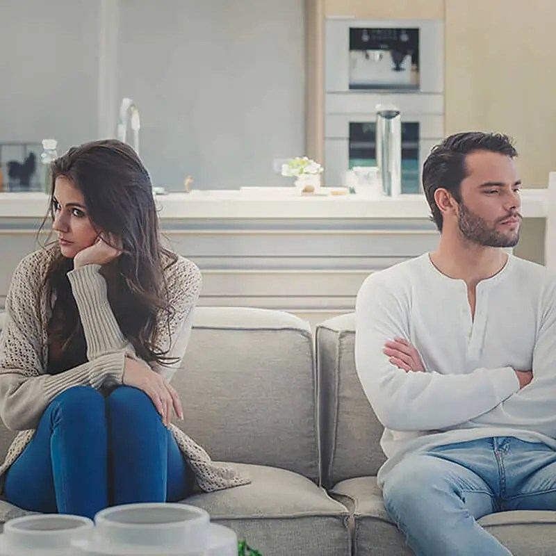 Couple sitting apart on couch appearing disconnected during relationship conflict