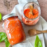 HERO Two glass mason jars filled with homemade marinara sauce are arranged on a light cloth with fresh basil leaves and wooden spoons v2