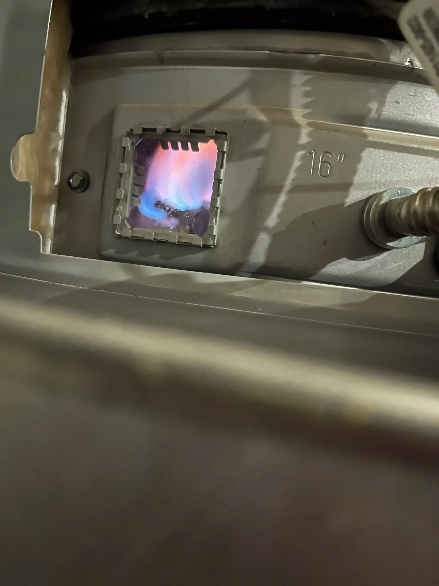 Active gas burner pilot flame inspected during a water heater installation in Austin