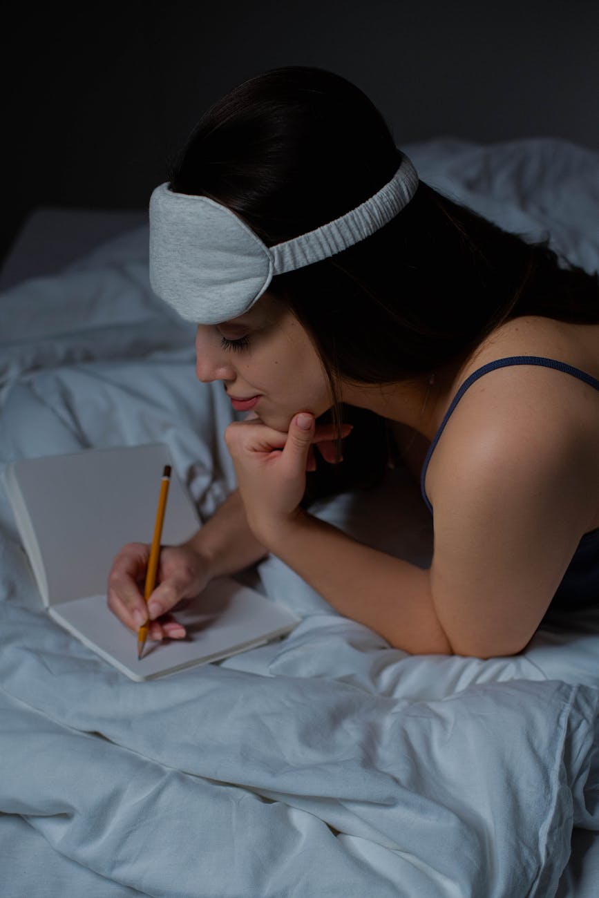 woman lying on front on bed writing on notebook