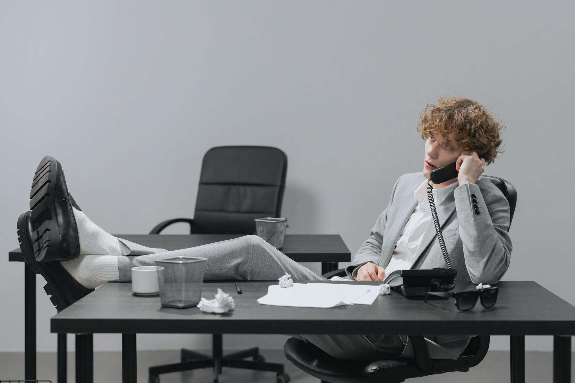 a man in gray suit sitting on the chair while talking on the phone