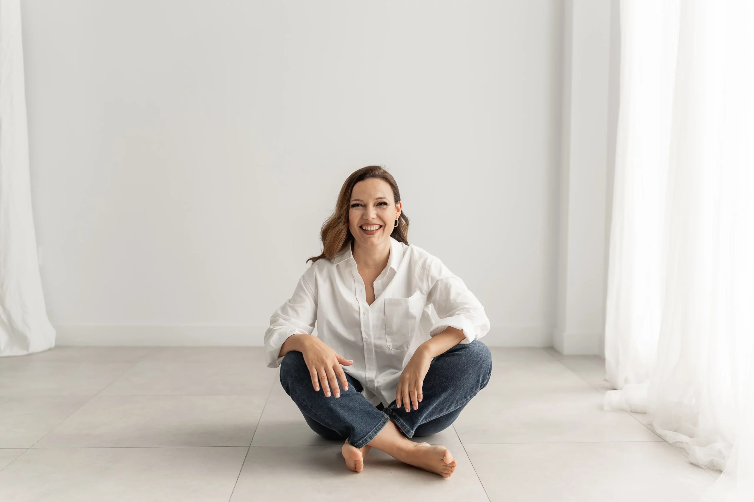 Retrato de la psicóloga Cristina Andrades sentada en el suelo sonriendo, con las piernas cruzadas, para su proyecto "El Sofá Turquesa".