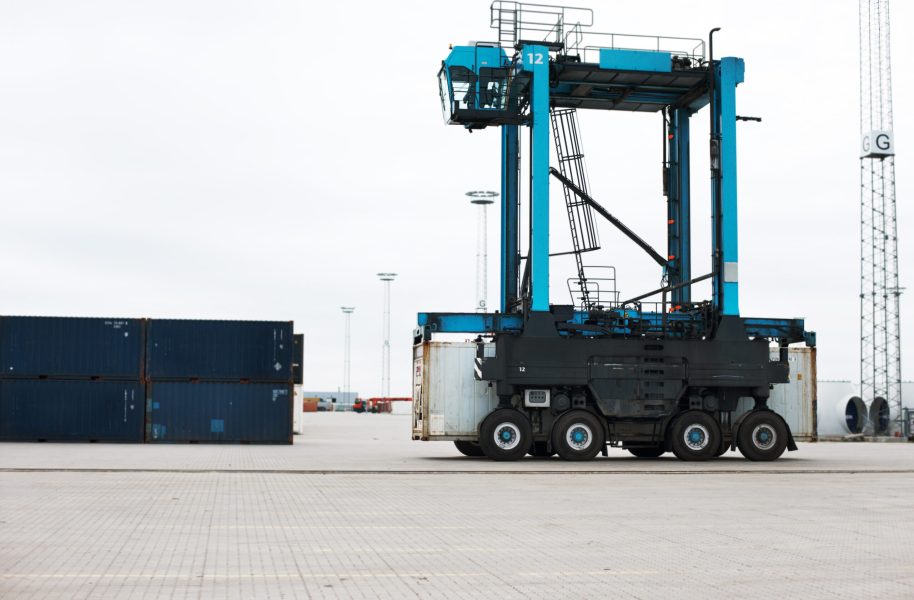 Shipping, cargo and logistics with straddle carrier for container, delivery and transportation at port. Freight, export and global stock with loading vehicle for economy, storage and industrial.