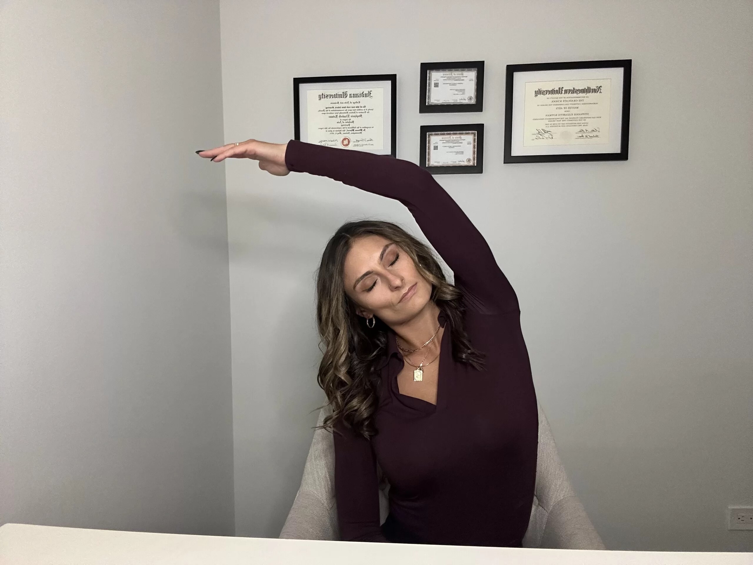 Professional woman seated at a desk practicing a side lateral stretch, a desk yoga pose to reduce tension, relieve stress, and enhance focus.