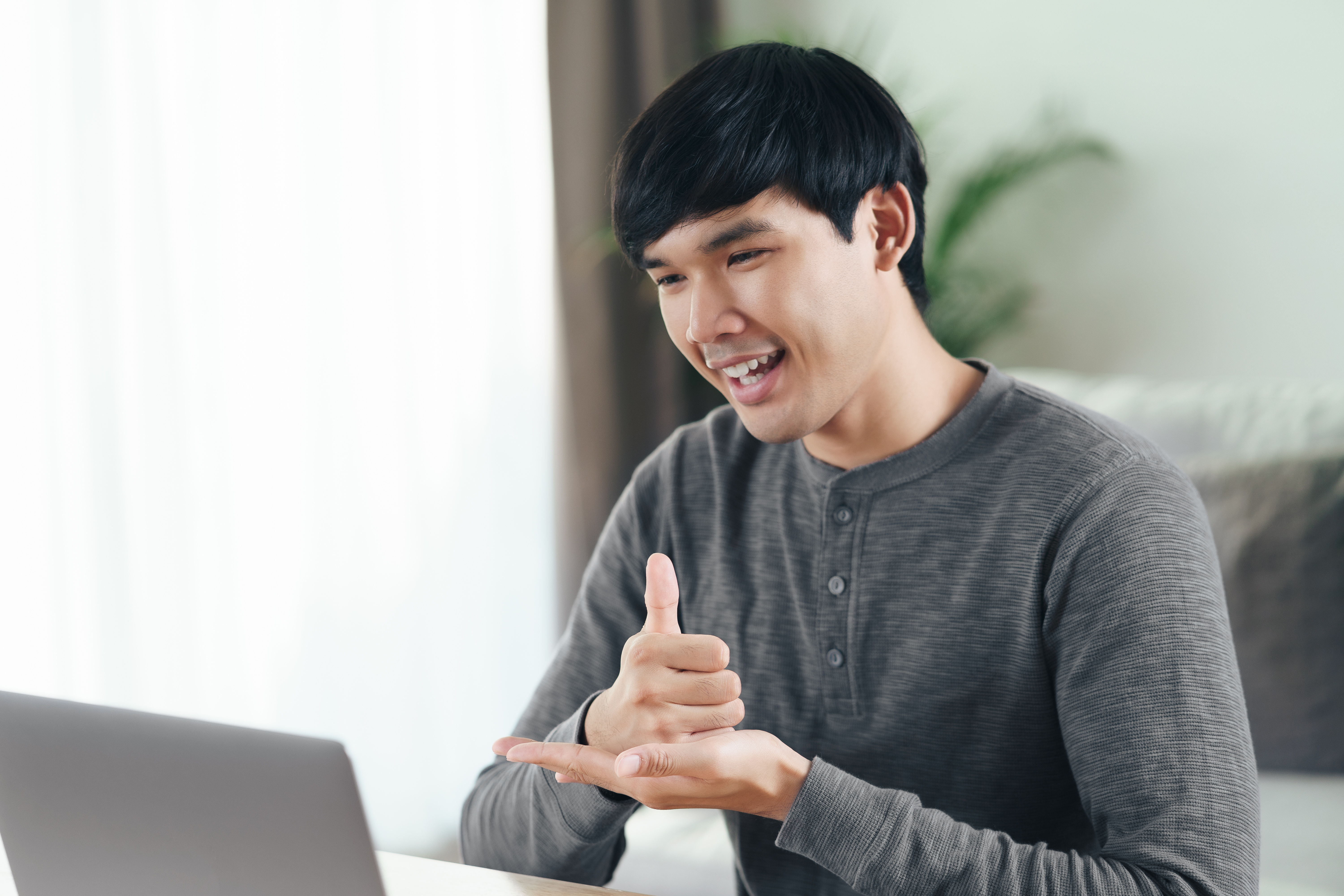 Young Asian man deaf disabled using laptop computer for online video conference call learning and communicating in sign language.