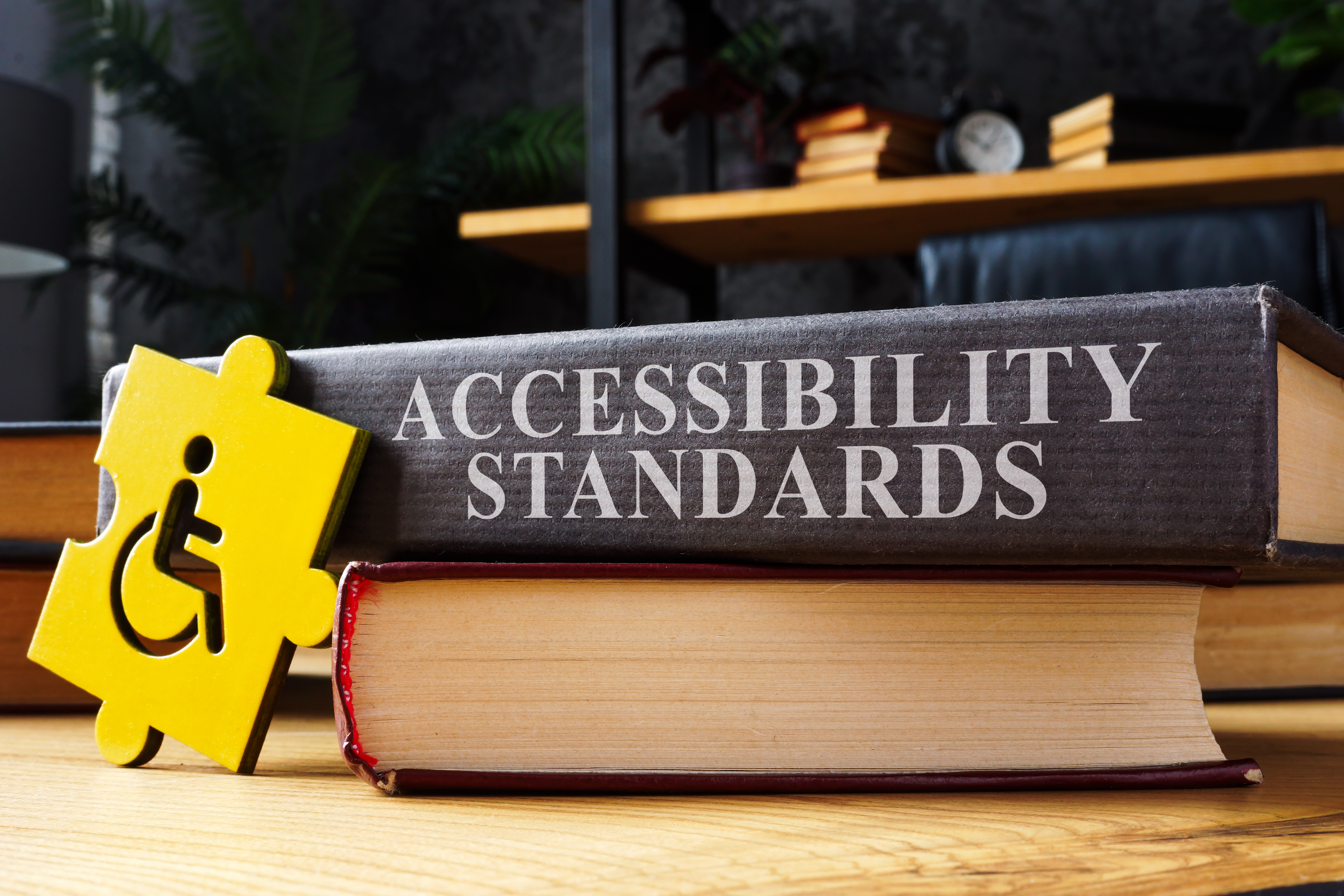 Accessibility standards book on a desk with the image of a body in a wheelchair on yellow puzzle piece leaning against it.