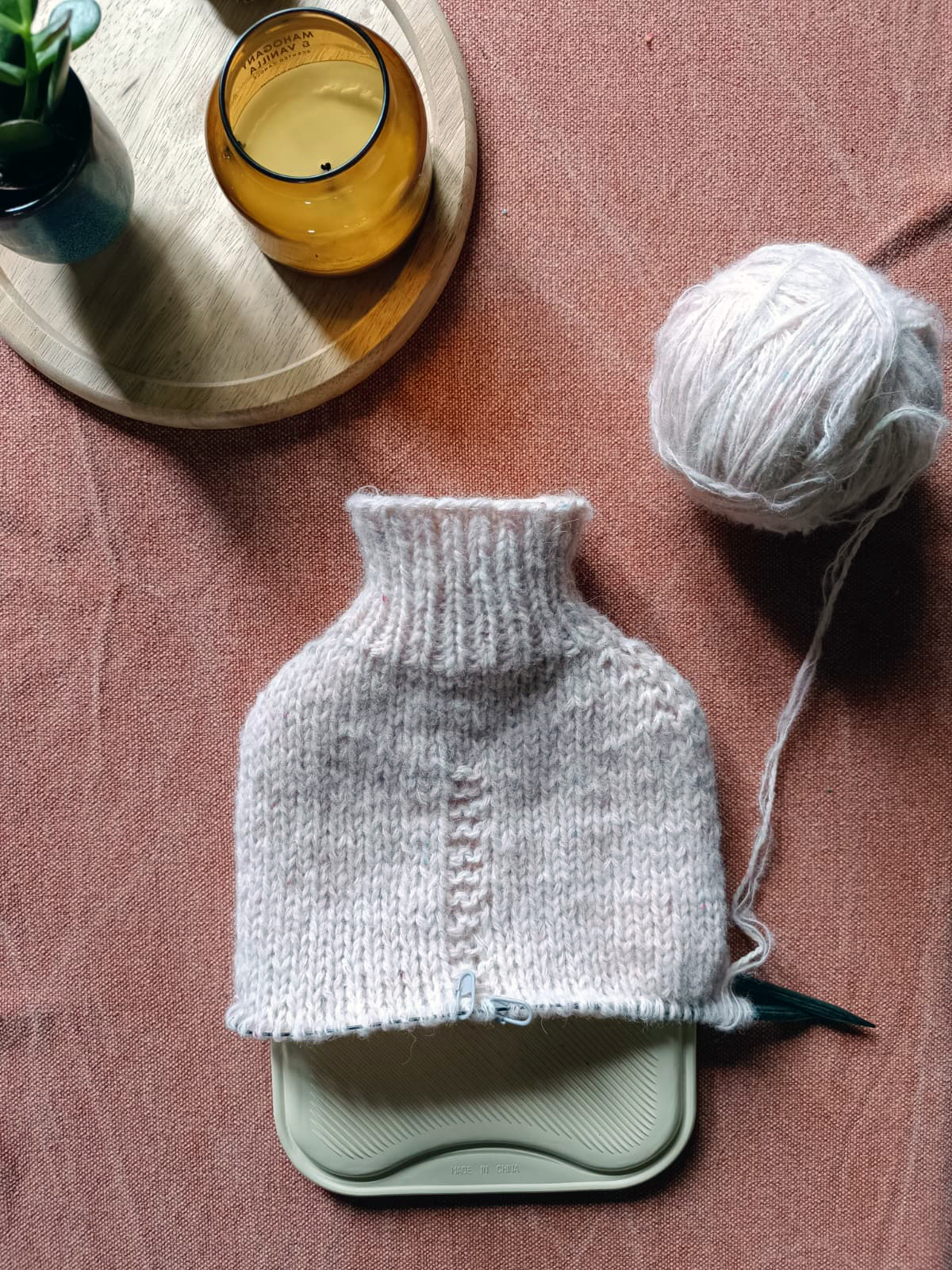Hand knitted light pink hot water bottle cover on a white background
