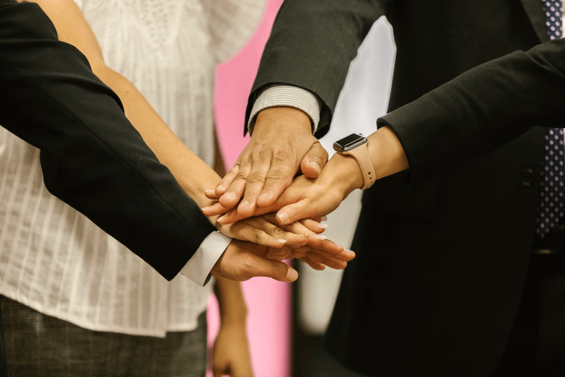 Group of business professionals stacking hands in a team huddle, representing corporate engineering culture