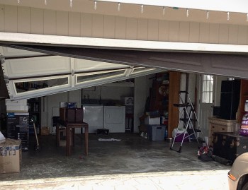 Image of crooked garage door hanging after cables have come off.